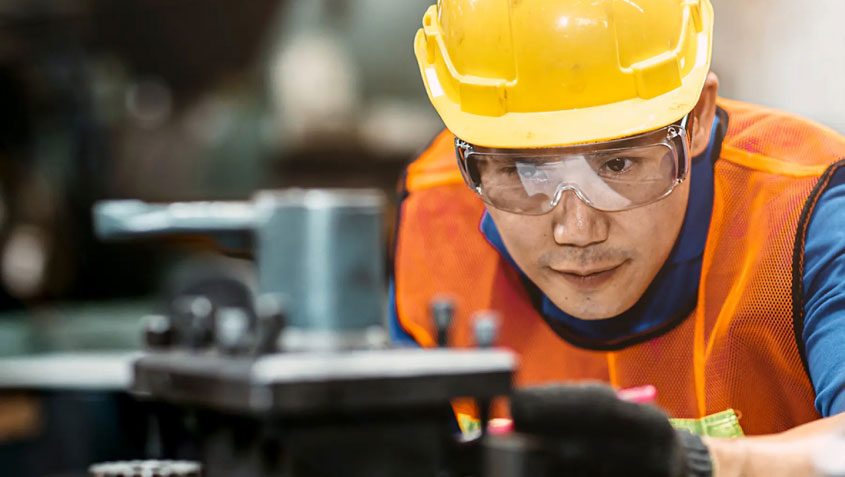 man with hardhat and orange vest working with machinery