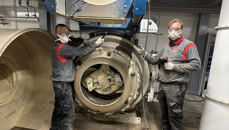 two men with face masks on, standing next to die machinery
